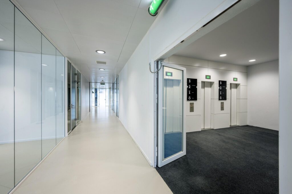 Modern hallway with glass walls leading to an elevator area at Prof. E.M. Meijerslaan.